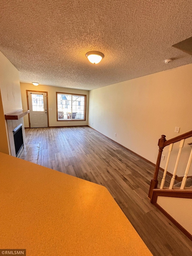 unfurnished living room with stairs, a textured ceiling, a tiled fireplace, and wood finished floors