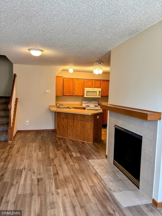 kitchen featuring brown cabinetry, light wood-style floors, white appliances, a peninsula, and baseboards