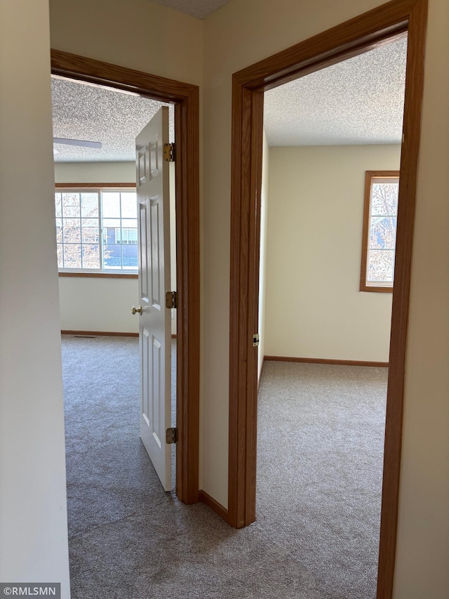 hall featuring carpet floors, a textured ceiling, and baseboards