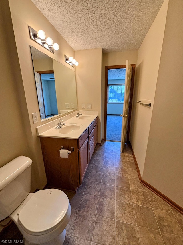 full bath featuring a textured ceiling, double vanity, a sink, and toilet