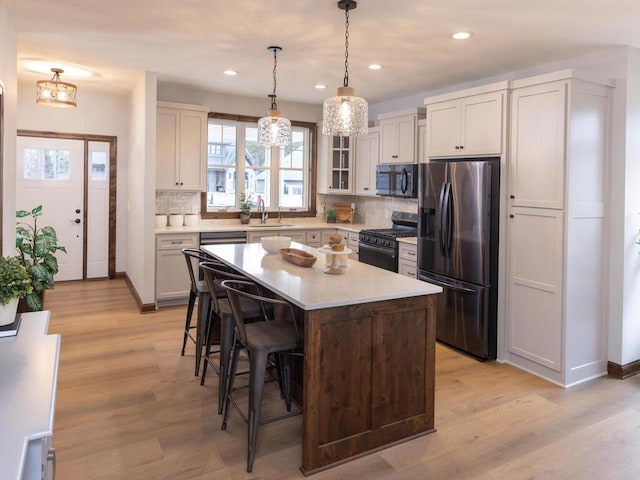 kitchen featuring black appliances, a breakfast bar area, light wood finished floors, and light countertops