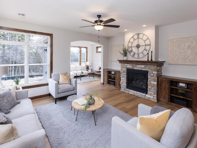 living room with arched walkways, recessed lighting, a fireplace, wood finished floors, and a ceiling fan