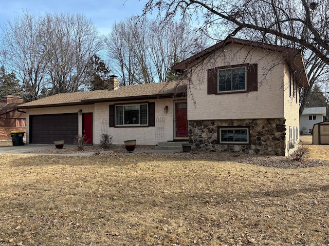 split level home featuring a shingled roof, a chimney, concrete driveway, a garage, and stone siding