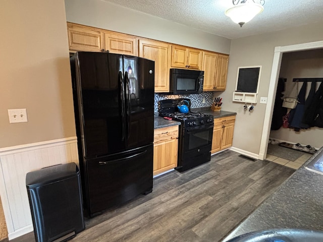 kitchen with a wainscoted wall, black appliances, dark wood-type flooring, a textured ceiling, and dark countertops