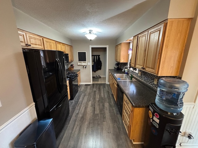 kitchen featuring dark countertops, backsplash, dark wood-style floors, black appliances, and a sink