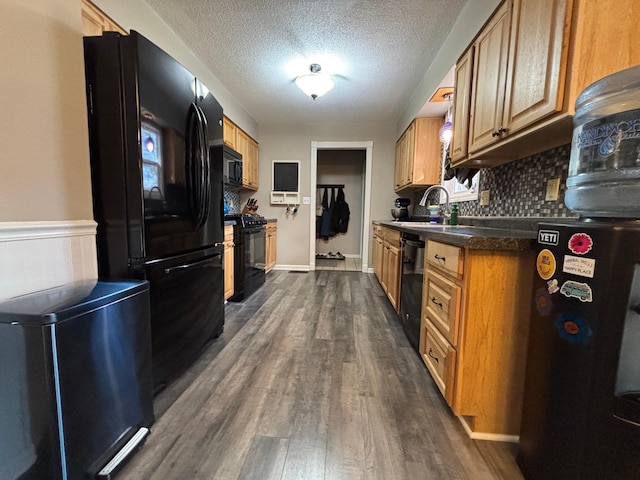 kitchen featuring dark wood-type flooring, black appliances, a sink, backsplash, and a textured ceiling