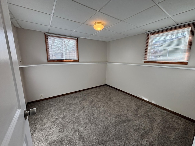 carpeted empty room featuring a drop ceiling, baseboards, and plenty of natural light