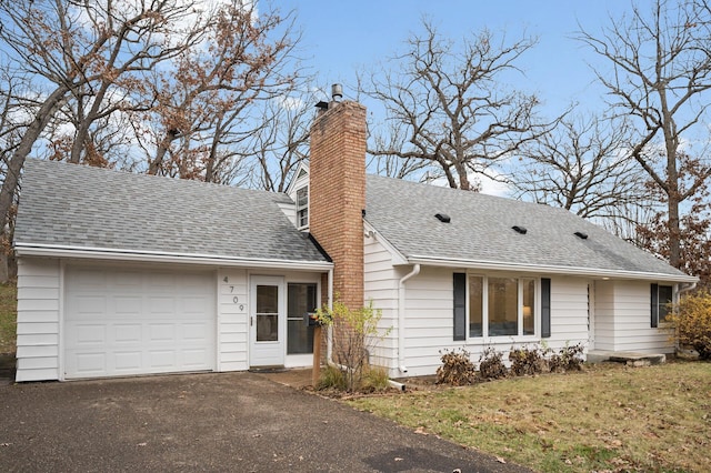 view of front facade featuring aphalt driveway, a chimney, a shingled roof, an attached garage, and a front yard