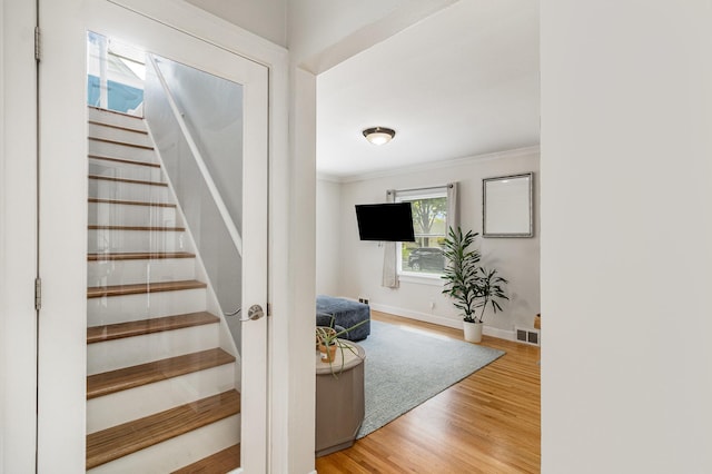 staircase with wood finished floors, crown molding, and baseboards
