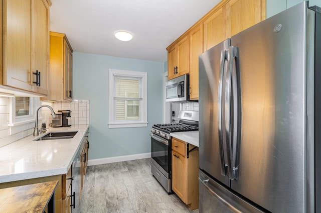 kitchen with appliances with stainless steel finishes, a sink, decorative backsplash, and light wood-style floors