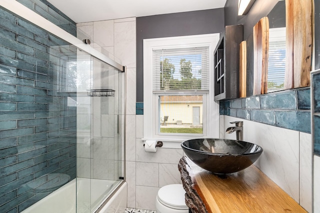 full bath with tile walls, plenty of natural light, bath / shower combo with glass door, toilet, and vanity