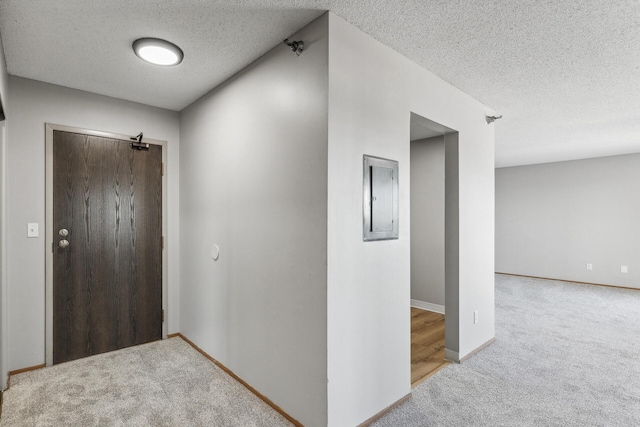 hall featuring a textured ceiling, carpet, electric panel, and baseboards