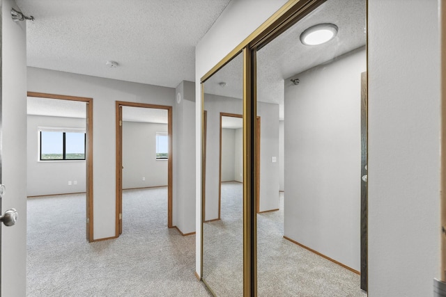 hallway with a textured ceiling, carpet flooring, and baseboards