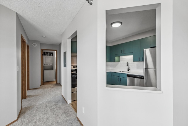 kitchen with a textured ceiling, light carpet, a sink, appliances with stainless steel finishes, and decorative backsplash