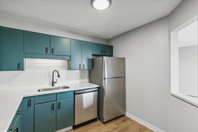 kitchen with appliances with stainless steel finishes, light wood-type flooring, light countertops, and a sink