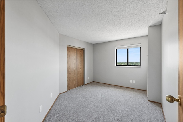 empty room with light carpet, a textured ceiling, and baseboards