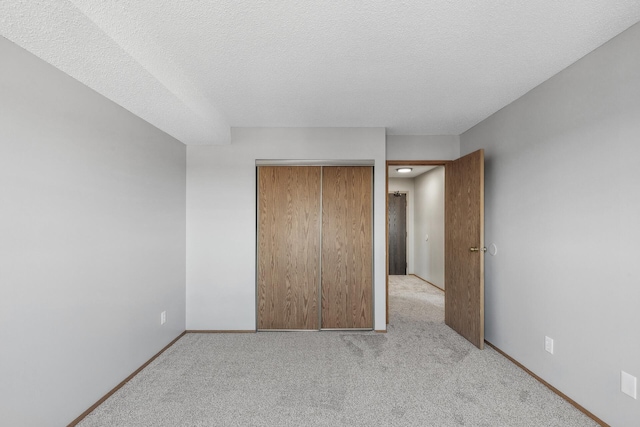 unfurnished bedroom with a closet, baseboards, a textured ceiling, and light colored carpet