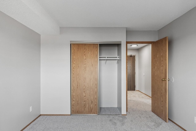 unfurnished bedroom featuring a closet, carpet flooring, a textured ceiling, and baseboards