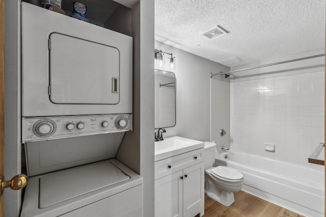 full bathroom featuring visible vents, stacked washer / dryer, toilet, wood finished floors, and a textured ceiling