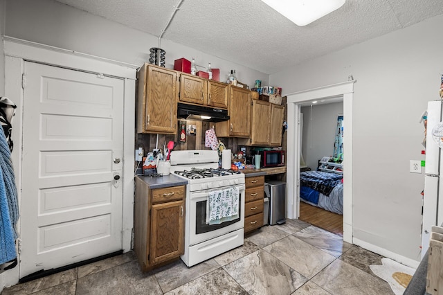 kitchen featuring under cabinet range hood, a textured ceiling, white gas range oven, black microwave, and brown cabinetry