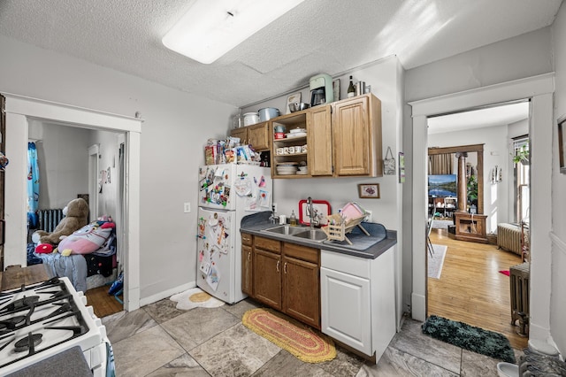 kitchen featuring white appliances, radiator, a sink, a textured ceiling, and dark countertops