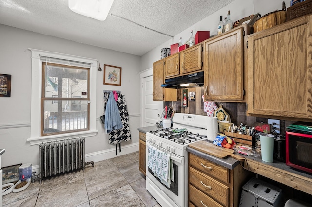 kitchen featuring radiator, baseboards, brown cabinets, under cabinet range hood, and white gas range