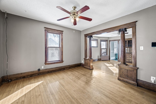 unfurnished room featuring decorative columns, baseboards, light wood finished floors, and a textured ceiling