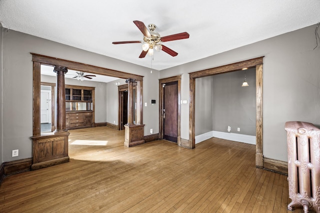 unfurnished room featuring hardwood / wood-style floors, radiator, decorative columns, baseboards, and ceiling fan