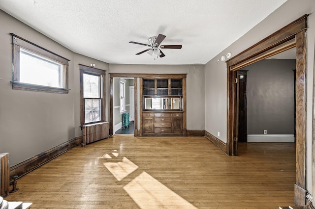 unfurnished room with radiator heating unit, wood finished floors, baseboards, and a textured ceiling