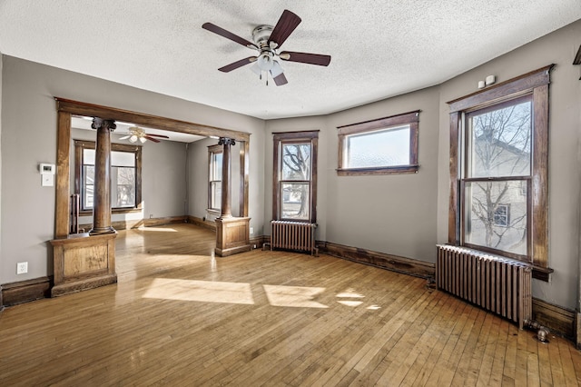 interior space with hardwood / wood-style flooring, radiator heating unit, baseboards, and decorative columns