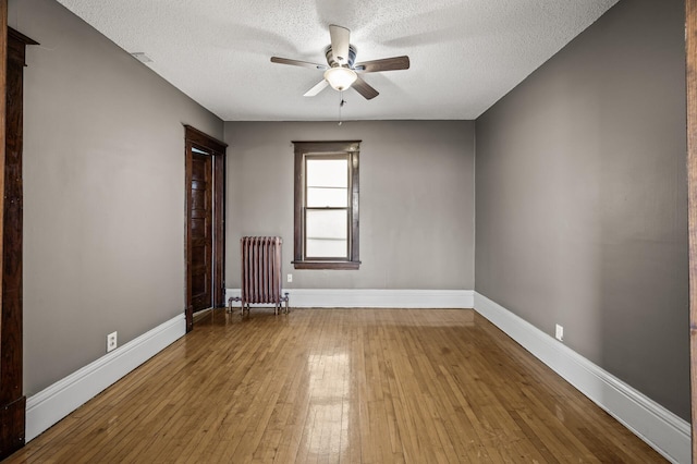 unfurnished room featuring baseboards, radiator heating unit, hardwood / wood-style flooring, a textured ceiling, and a ceiling fan