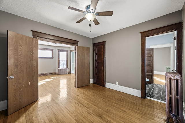 spare room with radiator, a ceiling fan, light wood-type flooring, and baseboards