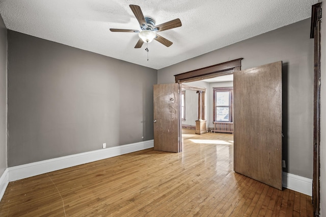 unfurnished room featuring ceiling fan, radiator, baseboards, and wood-type flooring