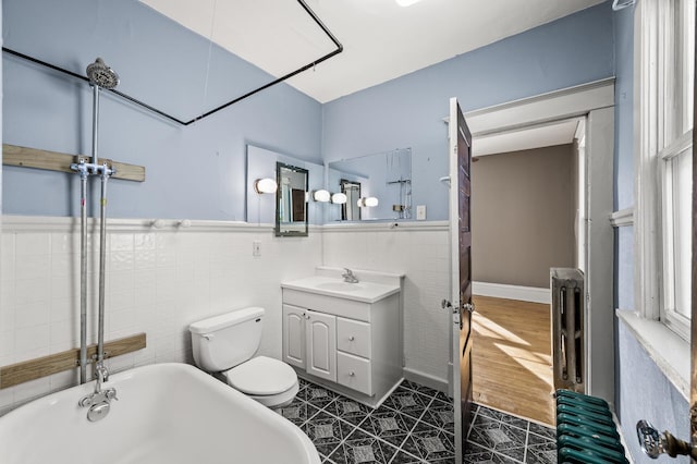 full bathroom featuring toilet, a washtub, tile walls, wainscoting, and vanity