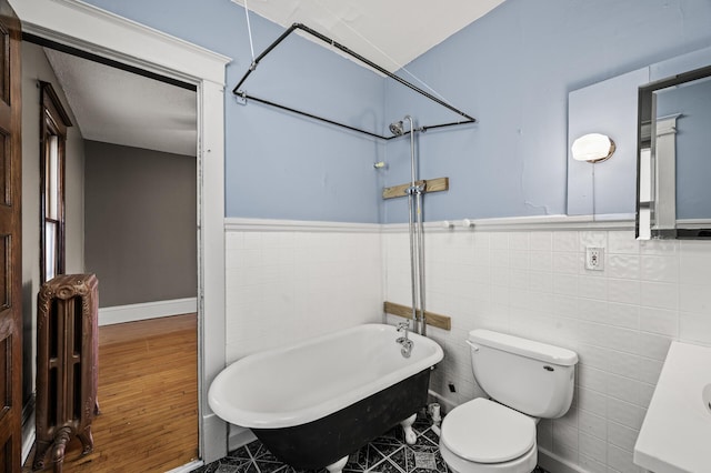 full bath with toilet, a freestanding bath, radiator heating unit, wainscoting, and tile walls