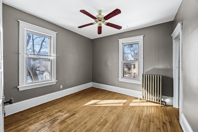 unfurnished room featuring a wealth of natural light, baseboards, wood-type flooring, and radiator heating unit