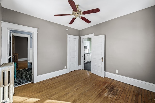 unfurnished bedroom with baseboards, radiator heating unit, ensuite bathroom, hardwood / wood-style flooring, and a ceiling fan