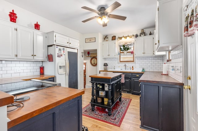 kitchen with wooden counters, light wood-style flooring, white cabinets, white refrigerator with ice dispenser, and tasteful backsplash