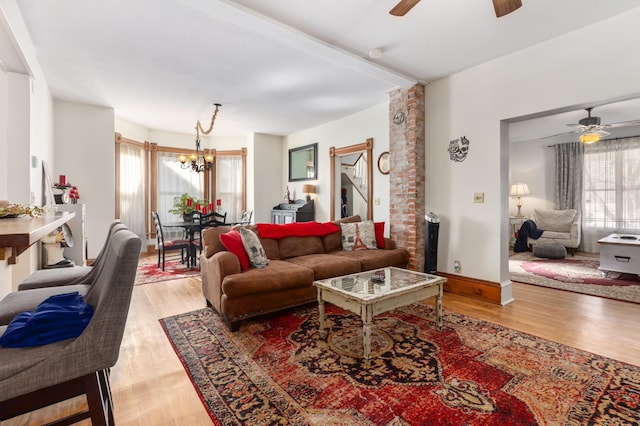 living room with ceiling fan with notable chandelier, baseboards, and light wood-style floors