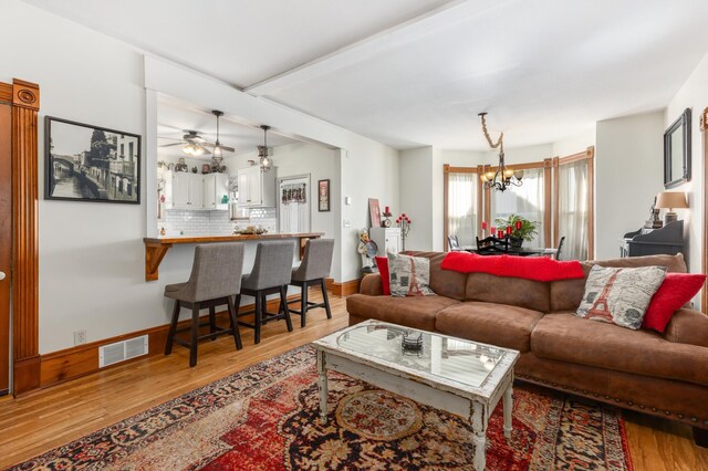 living room featuring visible vents, ceiling fan with notable chandelier, light wood-type flooring, and baseboards