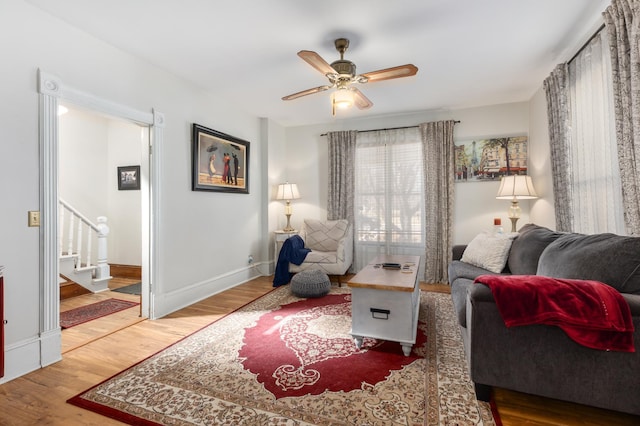 living room featuring stairway, ceiling fan, baseboards, and wood finished floors