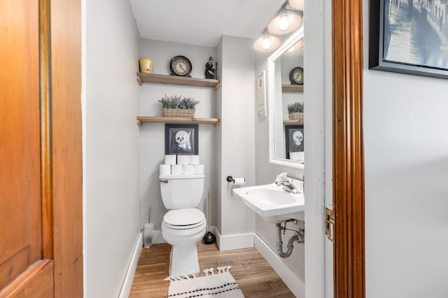 half bath with a sink, toilet, baseboards, and wood finished floors