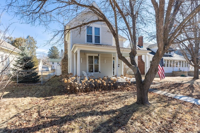 view of front facade with covered porch, a chimney, and fence