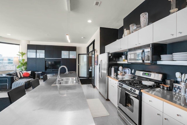 kitchen featuring stainless steel appliances, stainless steel countertops, visible vents, white cabinetry, and a sink