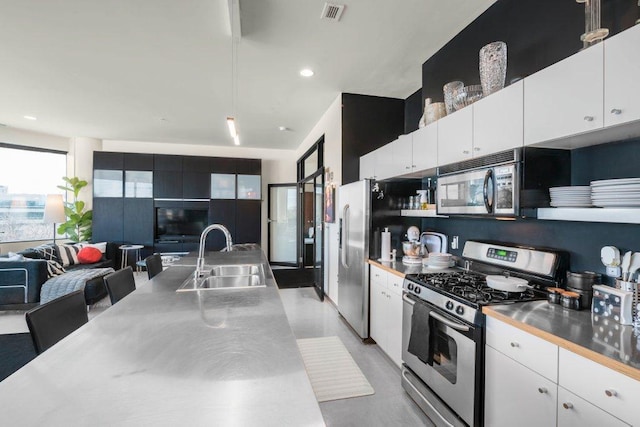 kitchen with white cabinets, a sink, stainless steel counters, stainless steel appliances, and visible vents