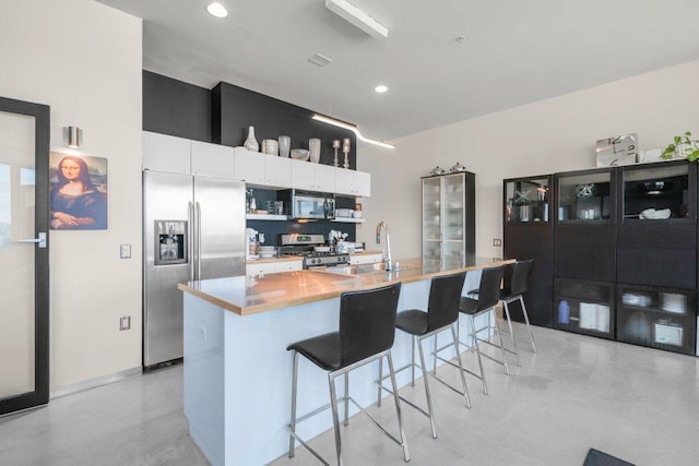 kitchen with a kitchen bar, appliances with stainless steel finishes, concrete flooring, white cabinets, and an island with sink