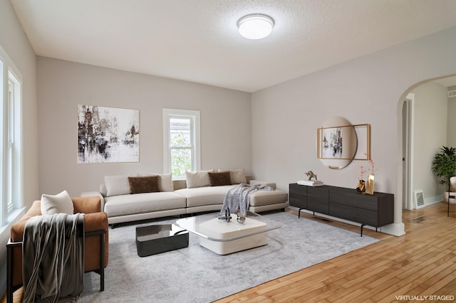 living area with a textured ceiling, arched walkways, and hardwood / wood-style floors