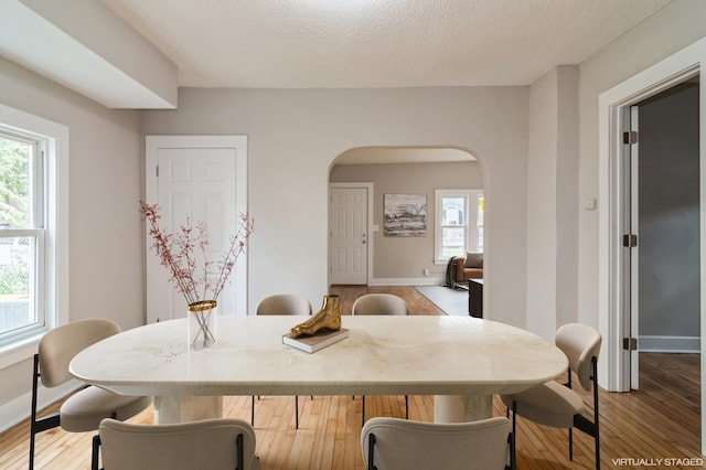 dining room with arched walkways, a textured ceiling, wood finished floors, and baseboards