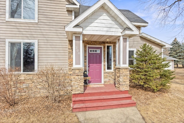 view of exterior entry featuring stone siding and roof with shingles