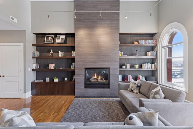 living room with built in features, wood finished floors, visible vents, a fireplace, and track lighting